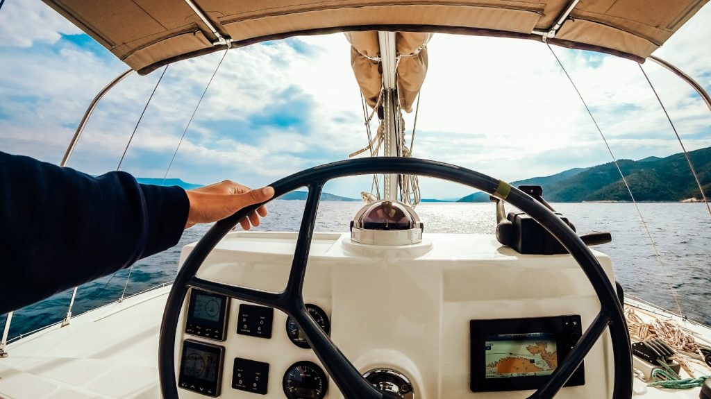 Mani sul volante di un barca, con un gps incorporato considerando . In lontananza si vede il cielo nuvoloso